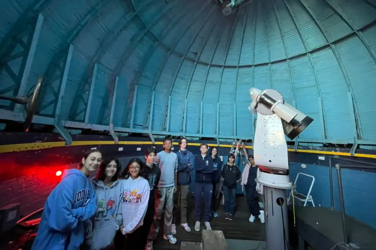 Ten high school students in a line around a large telescope in a round domed room.