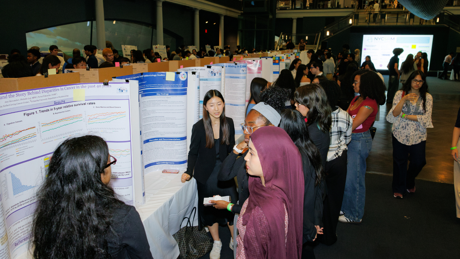 Large group of high-school-aged people surrounding a long line of tables with science project posters