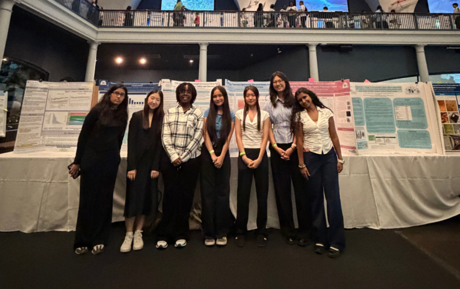 Seven high school students stand in front of science project posters at the American Museum of Natural History