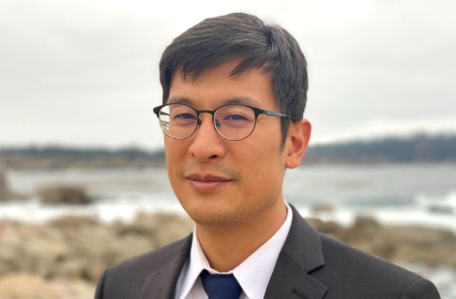 Headshot image of Columbia Professor James Chu in a suit, outdoors on a beach.