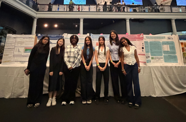 Seven high school students stand in front of science project posters at the American Museum of Natural History